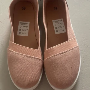 Sandaler Rosa  - Säljer ett par stilrena rosa loafers i textil med rund tå och vit sula.d Perfekta för en avslappnad look.