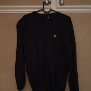 Mörkblå tröja från Lyle & Scott - Säljer en stilren mörkblå tröja från Lyle & Scott med deras ikoniska gula logga på bröstet. Tröjan har långa ärmar och en klassisk passform. Perfekt för en avslappnad men ändå snygg look.