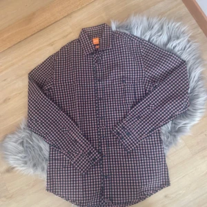 Rutig skjorta från Hugo Boss - Snygg rutig skjorta från Hugo Boss i blått, rött och vitt. Skjortan har en slim fit passform och är långärmad med knappar framtill. Perfekt för en stilren look.