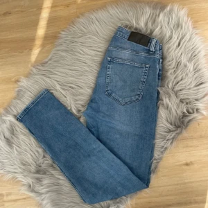 Blå jeans från Dressmann - Snygga blå jeans från Dressmann i slim fit-modell. Tillverkade av bomull med en liten del elastan för extra komfort. Klassisk design med fem fickor och knappgylf. Perfekta för en stilren look.