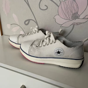 Vita sneakers med snörning - Snygga vita sneakers med klassisk design och snörning. Skorna har en rund tå och en blå rand längs sulan. Perfekta för en avslappnad stil.