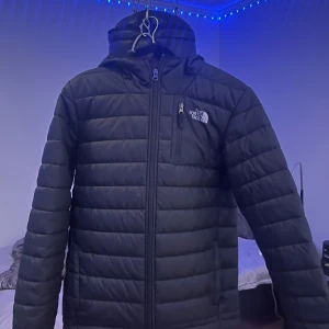Svart jacka från The North Face - Säljer en svart jacka från The North Face med dragkedja och huva. Jackan har en bröstficka med dragkedja och är perfekt för kyligare väder. Storlek XL junior men är stor i storlek så jag skulle säga den passa S-M i herr storlek. Skick: 10/10 aldrig använd.
