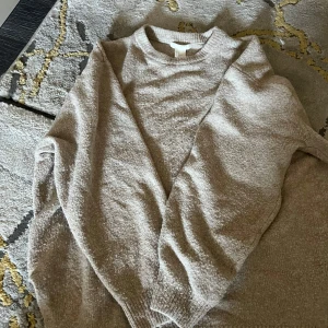 Beige stickad tröja - Säljer en mysig beige stickad tröja med rund hals och långa ärmar. Perfekt för kyliga dagar och enkel att matcha med olika outfits. Passar både till vardags och mer avslappnade tillfällen.