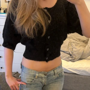 Svart stickad kofta från Lindex - Säljer en svart stickad kofta från Lindex med korta ärmar och knappar framtill. Perfekt för lager-på-lager och ger en mysig känsla. Passar bra till både jeans och kjol.