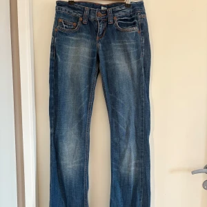 Blå jeans med broderade detaljer bootcut lowrise - Snygga blå jeans med broderade detaljer på bakfickorna och bältet. De har en klassisk femficksdesign och en knappgylf. Perfekta för en avslappnad stil. Mått: midja: 71 cm, innerben:80 cm 