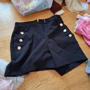 Svart skjorts från Amisu - Snygg svart skjorts från Amisu med dekorativa knappar i guld på framsidan. Skjortsen har en dragkedja bak för enkel på- och avtagning. Perfekt för att ge en stilren touch till din outfit.