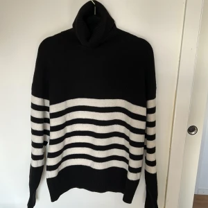 Svart och vit randig polotröja från Lindex - Säljer en snygg svart och vit randig polotröja från Lindex. Tröjan är tillverkad i en mjuk blandning av ull, polyester och akryl. Den har långa ärmar och en bekväm polokrage. Perfekt för kyliga dagar!