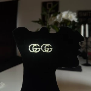 Guldiga örhängen med glittriga stenar - Snygga örhängen i form av dubbla G-bokstäver, dekorerade med glittriga stenar. Perfekta för att ge en touch av glamour till din outfit.