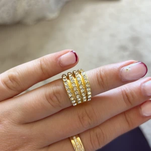 Guldig ring med glittrande stenar - Säljer en bred guldig ring med flera rader av gnistrande stenar som ger en riktigt lyxig känsla. Ringen har en cool staplad look och passar perfekt för dig som gillar att sticka ut med accessoarer.en sten har lostnat