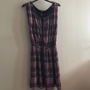 Mönstrad kort klänning från H&M - Snygg kort klänning från H&M med ett coolt mönster i svart, rött och vitt. Ärmlös modell med rund halsringning och resår i midjan som ger en skön passform. Perfekt för dig som gillar färg och mönster!