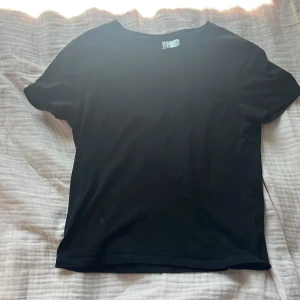 Svart basic t-shirt från H&M Divided - En svart basic t-shirt från H&M Divided i storlek S. Klassisk rund halsringning och korta ärmar. T-shirten är i mjuk bomull och har en enkel, clean look som funkar till allt. Perfekt för dig som gillar minimalistisk stil.