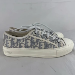 Dior sneakers i grått och vitt - Snygga walk n dior sneakers med grått och vitt monogrammönster, lågt skaft och vita snören. Skorna har en platt sula med 'Christian Dior J'Adior' präglat runt hälen. Tillverkade i textil med klassisk rund tå och stilren vibe. Har tyvärr ej fått kvitto därav priset men väldigt bra skick! 