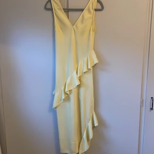 Ljusgul volangklänning från H&M - Supersöt ljusgul långklänning från H&M med v-ringning och ärmlös design. Klänningen har snygga volangdetaljer som går diagonalt över framsidan och ger en extra touch. Perfekt för sommarens alla tillfällen! Skulle säga att de är mer som en storlek s.💗