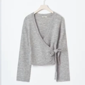 Grå omlottkofta från Ginatricot  - Säljer en mysig grå omlottkofta från Gina tricot. Koftan har en v-ringad design med knytning i sidan och långa ärmar. Perfekt för en stilren och bekväm look. Priset kan diskuteras vid snabb affär.