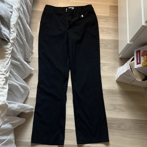 Svarta randiga kostymbyxor Madlady - Skit Snygga svarta kostymbyxor från Madlady i storlek 36. Byxorna har tunna vita ränder och klassisk rak passform. Perfekta för en clean och stilren look. Materialet känns mjukt och följsamt, och de har hällor för bälte samt knäppning framtill. Säljer på grund av att dem har blivit för små. 