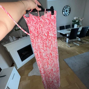 Långklänning med korall  mönster - Sommar klänning med knytning runt halsen .i jättefint skick med smala axelband och elastisk smock upptill. Klänningen har ett unikt korall och vitt mönster som ger en fräsch sommarkänsla. Perfekt för varma dagar och enkel att styla med sandaler eller sneakers.
