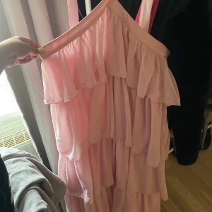 Ljusrosa volangklänning med axelband -  Klänningen har en flowy och romantisk look, perfekt för sommarens alla tillfällen. Materialet känns lätt och luftigt. Använd en gång. Passar perfekt till fina tillställningar ä. Storlek L men det är mer utav en M