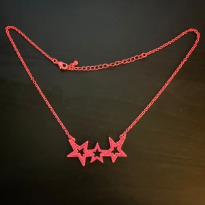 Rosa halsband med stjärnor - Coolt halsband i starkt rosa med tre sammankopplade stjärnor som hänge. Stjärnorna har glittriga detaljer och kedjan är tunn och justerbar. Perfekt för dig som vill sticka ut med ett färgglatt och lekfullt smycke.