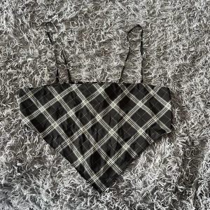 Svartvit rutig bandana-topp H&M Divided - Säljer en svartvit rutig bandana-topp från H&M Divided i storlek L. Topp med smala axelband, elastisk smock baktill och spetsig nederkant framtill. Tillverkad i mjuk polyester med lite stretch för skön passform. Perfekt för en trendig look!