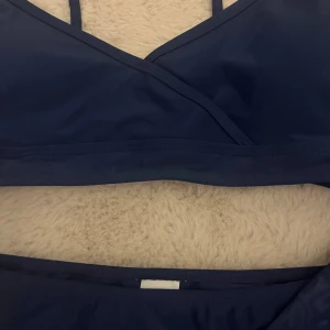 Mörkblå bikini från SHEIN - Snygg mörkblå bikini från SHEIN med fin och smala axelband. Klassisk bikiniunderdel och matchande meshkjol. Perfekt för stranden eller poolen, enkel och stilren design. Materialet är stretchigt och bekvämt. Aldrig använd och säljer eftersom jag inte använder och är för liten!