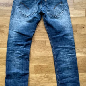 Dondup jeans - Säljer ett par blå jeans med snygga slitningar och tvättade detaljer. Jeansen har raka ben, klassiska bakfickor med dekorativa sömmar och orange kontrastsömmar. Materialet är jeans och passformen är straight