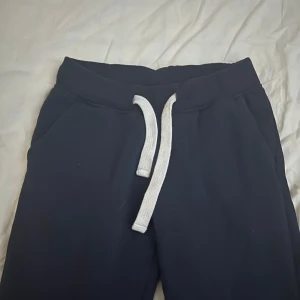 Mörkblå mjukisbyxor från russemerch - Mörkblå mjukisbyxor med bred resår i midjan och vit snörning framtill. Byxorna har raka ben och är gjorda i mjukt material. Säljer för att dem har blivit för korta, använd två gånger