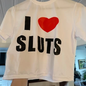 Vit t-shirt med tryck i XXL - Vit t-shirt  med stort tryck på framsidan: 'I ❤️ SLUTS' i svart och rött. Klassisk rund hals och korta ärmar. T-shirten är rak i modellen och har en enkel, clean look. Perfekt för dig som gillar statement-plagg. Påstås vara XXL skulle säga en M som störst och har man stora bröst sitter den som en bröst topp och inte magtröja 