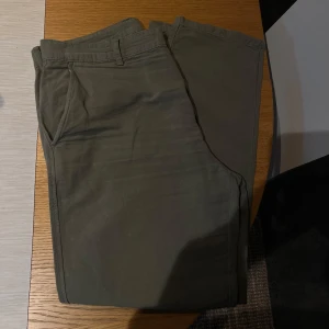 Olivgröna linnebyxor med normal passform - Snygga olivgröna chinos med klassisk design och raka ben. Byxorna har hällor för bälte, snedställda fickor fram och är tillverkade i mjuk bomull. Perfekta för en clean och avslappnad look.