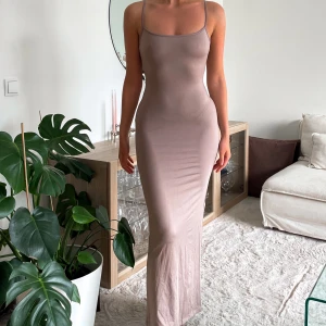 Beige långklänning med smala axelband - Supersnygg långklänning i beige med smala justerbara axelband och figurnära passform. Ryggen är urringad och djup. Endast testad med lappen kvar.