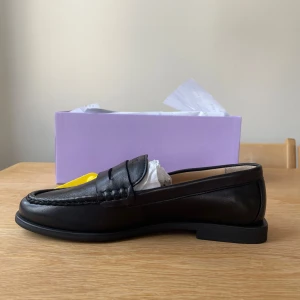 Svarta loafers från Copenhagen Studios - Stilrena svarta loafers i skinn från Copenhagen Studios. Klassisk penny loafer-design med rund tå, diskret söm längs kanten och präglad logga på ovandelen. Snygg och tidlös modell som passar till allt. Platt sula och bekväm passform. Oanvända i storlek 39. Nypris 2000kr - kap!