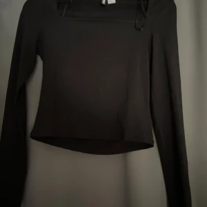 Svart långärmad topp från H&M - En svart långärmad topp från H&M med fyrkantig ringning och croppad passform. Enkel och stilren design som passar perfekt till jeans eller kjol. Mjuk och stretchig känsla, vilket gör den riktigt bekväm att bära. Storleken tycker jag känns mindre än storlek S, de känns mer som typ XS