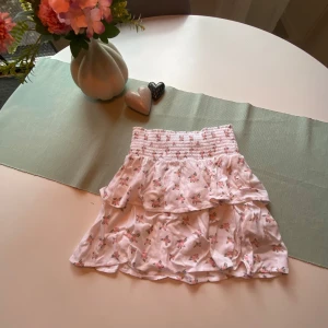 Vit blommig volangkjol  - Supersöt kort volangkjol från lager 157 i vit bomull med små rosa blommor. Kjolen har smock i midjan och dubbla volanger som ger en riktigt gullig och somrig vibe. Perfekt för dig som gillar romantisk och feminin stil. Pris går absolut att diskutera!❤️