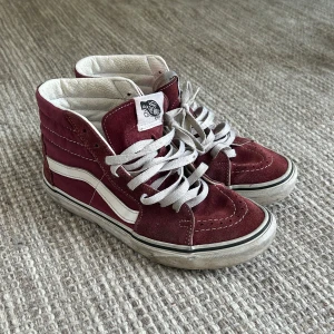 Vinröda Vans Sk8-Hi sneakers - Säljer ett par klassiska Vans Sk8-Hi sneakers i vinrött med vita detaljer och snörning. Skorna har en hög modell. 
