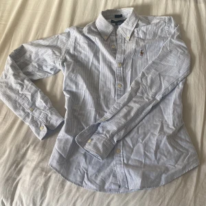 Ralph lauren skjorta - En riktigt stilig ralph lauren skjorta med blåa ränder och ett broderat märke. Perfekt nu i sommar med varma temperaturer! Viktigt att notera att den är slim så det kan sitta tajt. Passar därför också xs☀️⛱️👔