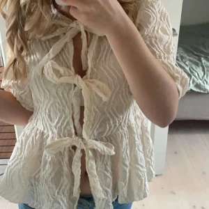 Beige blus med knyt från Gina Tricot - Supersöt beige blus från Gina Tricot i storlek XS. Blusen har tre knyt framtill, korta ärmar. Säljer pågrund av ingen användning. Endast använd 1 gång!!💕tveka inte att skriva om du har några frågor