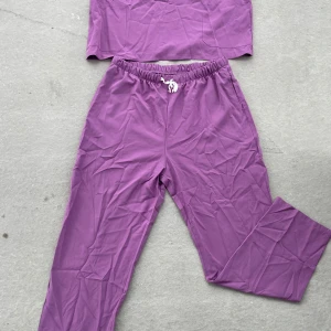 Lila byxor med snörning med tillhörande t-hirt - Säljer ett par lila mjukisbyxor med resår och vit snörning i midjan med tillhörande T-shirt. Byxorna och t-shirten har en relaxed passform och är gjorda i mjukt material, perfekta för chill dagar. Färgen är en snygg lila ton som sticker ut.