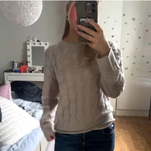 Beige stickad tröja med kabelmönster - Säljer en beige stickad tröja med klassiskt kabelmönster. Tröjan har rund halsringning och långa ärmar, perfekt för lager-på-lager under kyliga dagar. Enkel och stilren design som passar till jeans eller kjol.