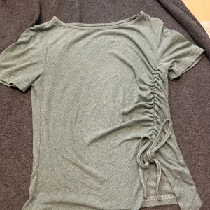 Ljusgrön ribbad topp med snörning - Snygg ljusgrön ribbad topp med kort ärm och trendig snörning på ena sidan. Toppen har en lätt croppad passform och är tillverkad i mjukt, stretchigt material som sitter skönt på kroppen. Perfekt för dig som gillar en enkel men ändå unik stil.