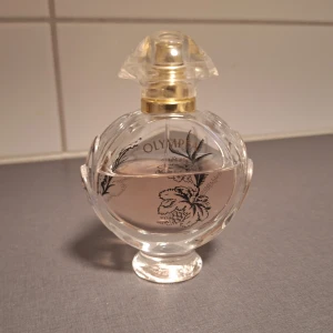 Paco Rabanne Olympéa Parfym - Säljer en lyxig Olympéa parfym från Paco Rabanne. Flaskan är rund i genomskinligt glas med guldiga detaljer och svart dekorlock. Doften är fruktig, rosig och blommig med inslag av vanilj, mysk och mjuka kryddor. Perfekt för dig som gillar eleganta och feminina dofter.