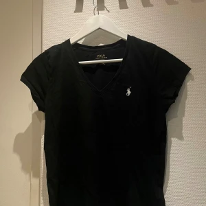 Svart t-shirt Polo Ralph Lauren - Svart t-shirt från Polo Ralph Lauren med klassisk v-ringning och korta ärmar. Ikoniska broderade loggan i vitt på bröstet. Tillverkad i mjuk bomull. Unisex.