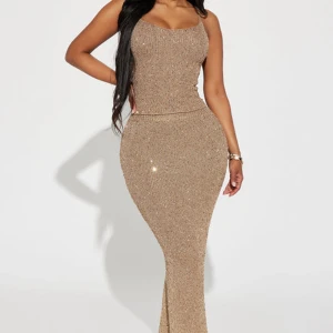Glittrig lång co-order i champagne - Supersnygg lång co-order i champagnefärg med smala axelband och figurnära passform. Glittrig och har en ribbad struktur som ger extra effekt. Perfekt för dig som vill sticka ut och glänsa på festen!