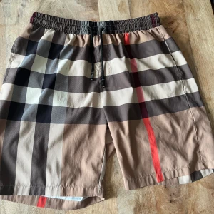 Burberry shorts - Snygga shorts från Burberry.  De har elastisk midja med svart snörning och är tillverkade i ett lätt och bekvämt material, perfekt för sommaren. Dom passar typ alla storlekar på grund av att midjan är elastisk. Köpte dom av en kompis för 1800 kr