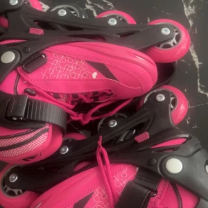 Rosa inlines med hjärtan och snörning - Snygga rosa inlines från Deltaport med vita hjärtan och grafiskt mönster. Skorna har snörning, kardborreband och spänne för extra bra passform. Yttermaterial i syntet och mesh, svarta detaljer och robusta hjul. Perfekta för dig som vill sticka ut på gatan! Storlek 29-33 pris kan diskuteras. Inlines+skydd. Kunden står för frakt 