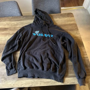 Svart Volvo hoodie Fruit of the Loom - Svart hoodie med huva och snörning från Fruit of the Loom. Framsidan har blått Volvo-tryck och baksidan har stort vitt och blått tryck med texten 'FUCK YOU I DRIVE A VOLVO'. Klassisk känguruficka framtill och ribbade muddar. Skick enligt bild