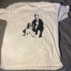 Vit t-shirt med tryck från Fruit of the Loom - Vit t-shirt från Fruit of the Loom i bomull med svart tryck av en man och en hund på framsidan. Klassisk passform och rund hals. Perfekt för dig som gillar unika motiv och vill sticka ut lite extra.
