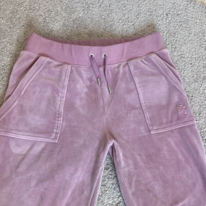 Rosa velourbyxor Juicy Couture S - Nypris: 1200kr, Mysiga rosa mjukisbyxor från Juicy Couture i velour med broderad JC-logga framtill, bred resår och snörning i midjan. Stora fickor fram och bak med tryckknappar. Färgen säljs inte mer och kan tyvvär inte hitta vad den heter.