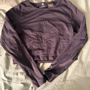 Mörkblå ribbad långärmad topp - Säljer en lila ribbad långärmad topp från Move. Tröjan är croppad och har en snygg, enkel design med rund halsringning. Perfekt att matcha med höga jeans eller kjol för en chill och trendig look.