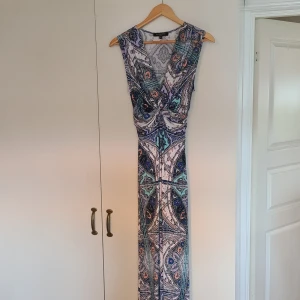 Mönstrad långklänning från  Ilse Jacobsen i storlek M - Säljer en långklänning från Ilse Jacobsen i storlek M, med färgstarkt paisleymönster i blått, mintgrönt, lila, vitt och persika. Klänningen är ärmlös, har v-ringning och snygg twist-detalj framtill. Materialet är mjukt , följsamt och stretchigt !