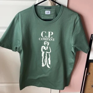 C.P. Company tshirt  - Snygg grön t-shirt från C.P. Company med vit tryckt logga och grafiskt motiv på bröstet. Tillverkad i 100% merceriserad bomull för en mjuk och lyxig känsla. Klassisk passform och rund hals. Tröjan är bara använd en gång då den är för stor för mig, skick 10/10. Köpt på nk för 1600, mitt pris 850kr. Hör av er vid mer frågor.