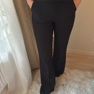 Svarta bootcut kostymbyxor - Snygga svarta kostymbyxor med bootcut-snitt och hög midja. Byxorna har en klassisk look med pressveck och sitter riktigt bra över höfterna. Perfekta för dig som gillar en stilren och trendig vibe.